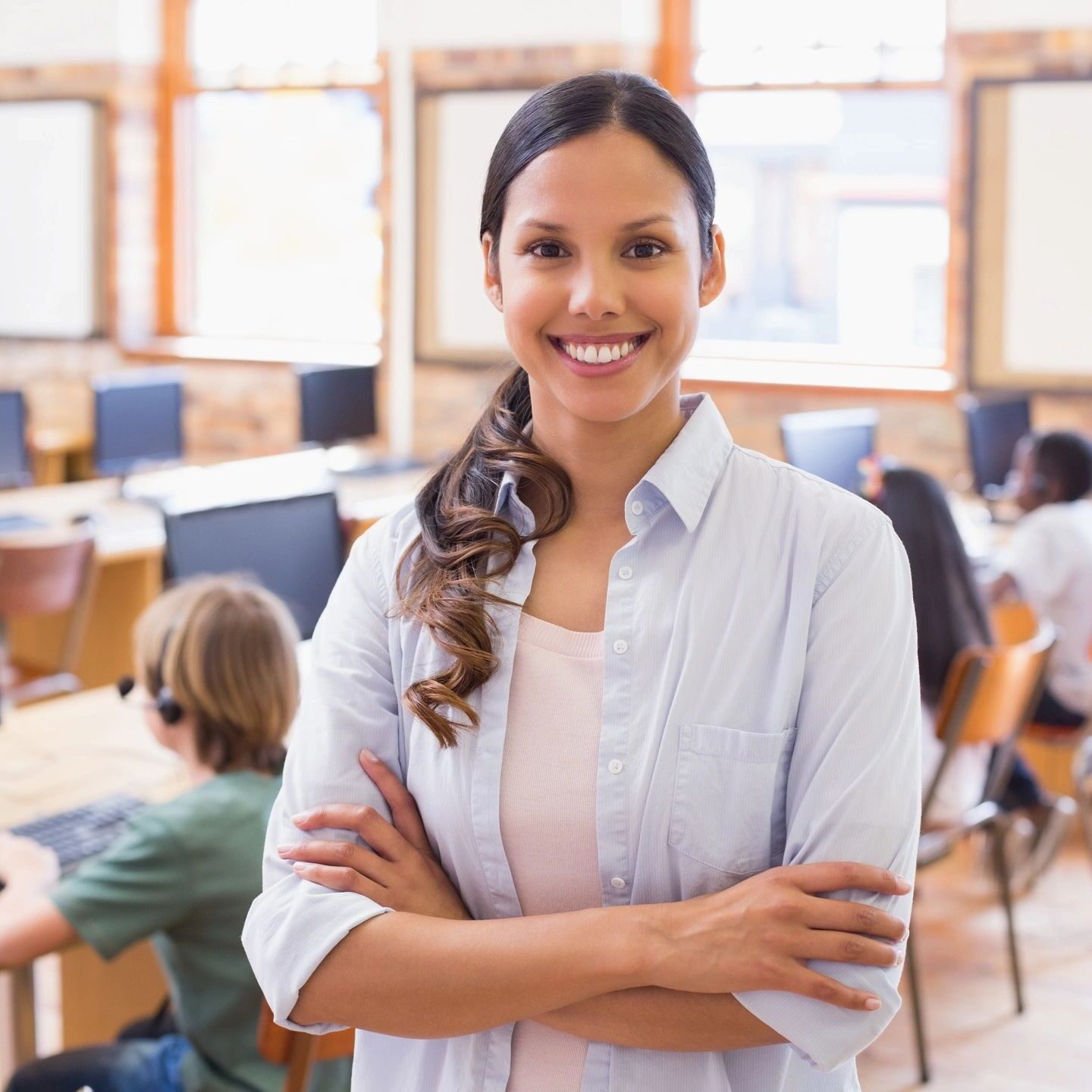 Confident woman standing with arms crossed in a busy office.