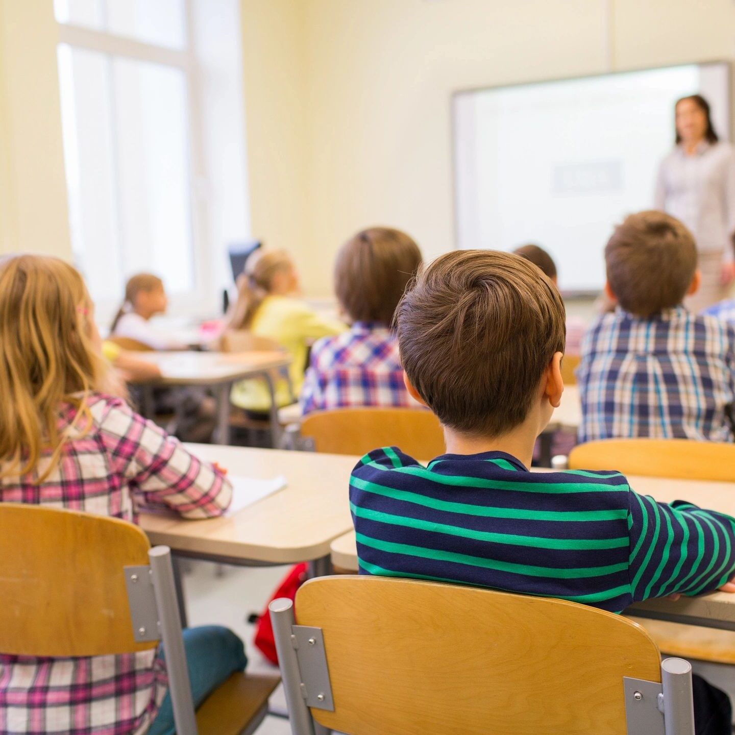 Students attentively listen to a teacher in a bright classroom.